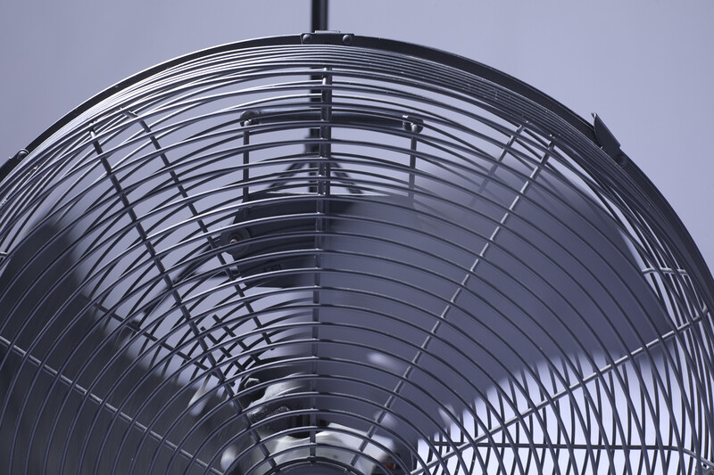 Close-up of a metal fan's grille and blades shot from directly below against a gray sky.