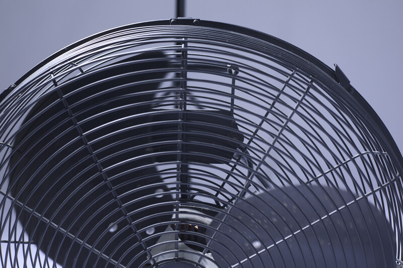 Close-up of a metal fan's grill and blade structure photographed from below against a light sky.