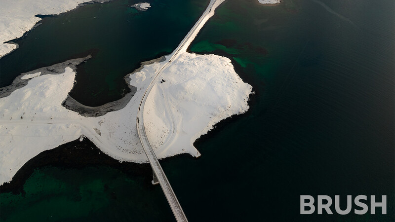 Aerial view of a curved road crossing white salt flats and dark water channels.