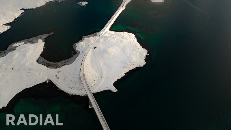 Aerial view of a curved road crossing white salt flats surrounded by dark water.