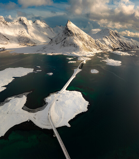 Snow-covered mountains and glacial islands separated by dark water in arctic landscape.