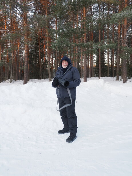 Person in dark winter clothing jogging through deep snow with coniferous forest background.
