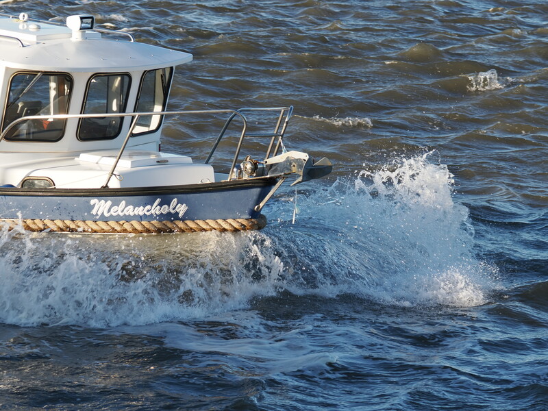 White fishing boat named Melancholy navigating through large ocean waves in bright daylight.