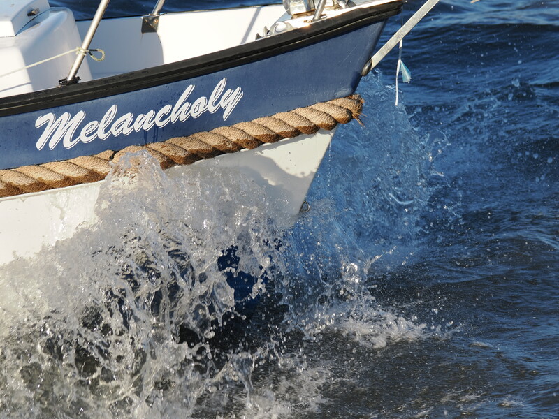 White fishing boat named Melancholy with rope and white water splash alongside hull.