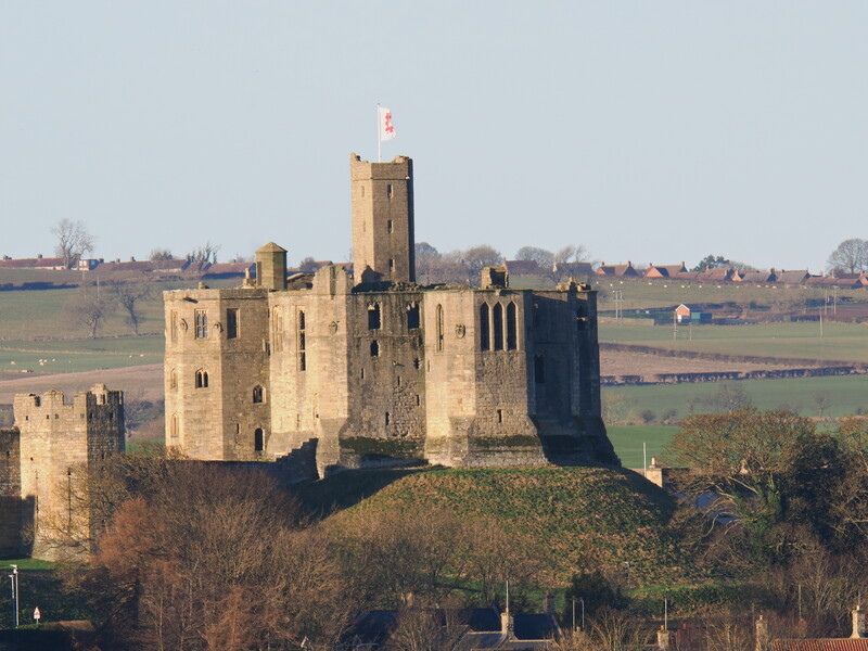 Medieval stone castle with central keep tower on elevated terrain overlooking countryside farmland.