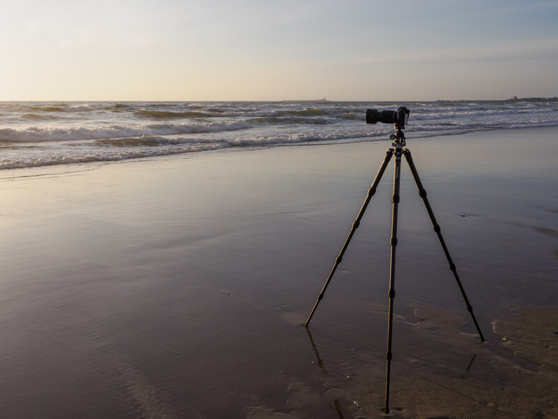 Camera on tripod set up in shallow ocean water during golden hour with waves and beach in background.