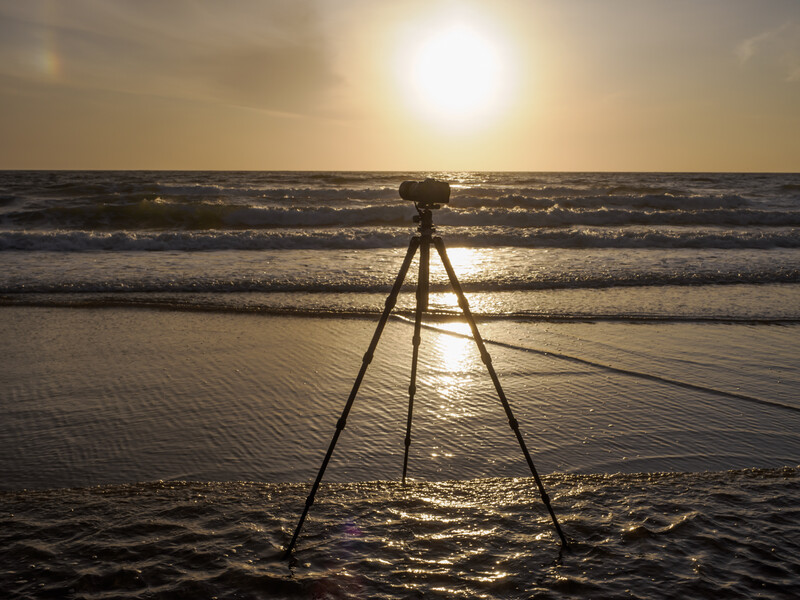 Camera mounted on tripod in shallow ocean water during golden hour sunset.