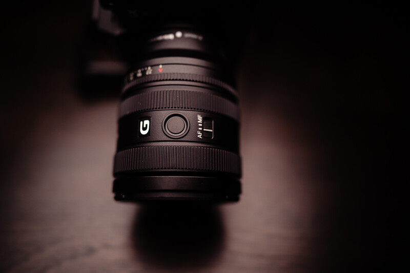 Close-up of a prime lens with focus ring and aperture markings against a dark, blurred background.