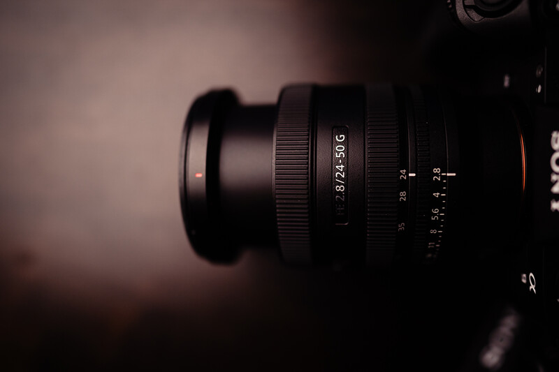 Close-up of a vintage manual focus lens with aperture and focus rings visible against a soft, blurred warm background.