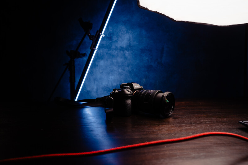Professional camera with attached lens on wooden surface, illuminated by blue neon light and a white overhead source.