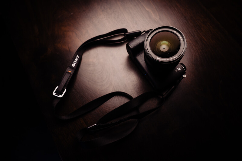 DSLR camera with wide-angle lens and black shoulder strap on dark wooden surface.