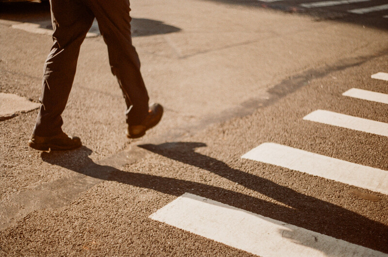 Person's legs and shadow crossing a zebra crossing on asphalt in bright sunlight.