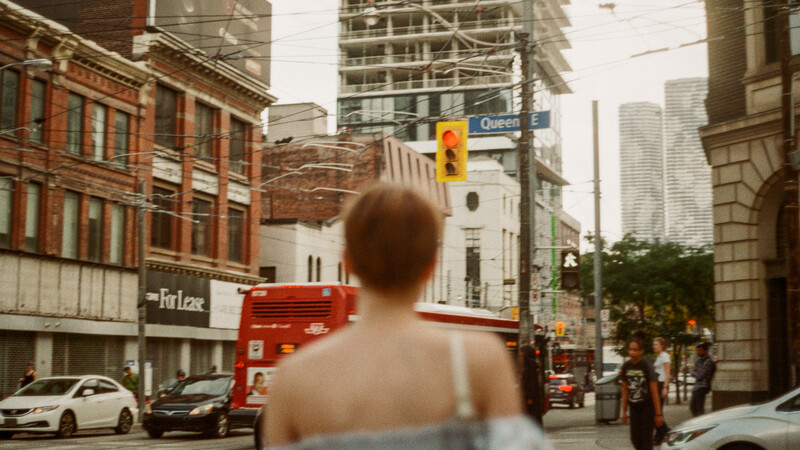 Shirtless person from behind facing an urban street intersection with historic brick buildings and modern skyscrapers.