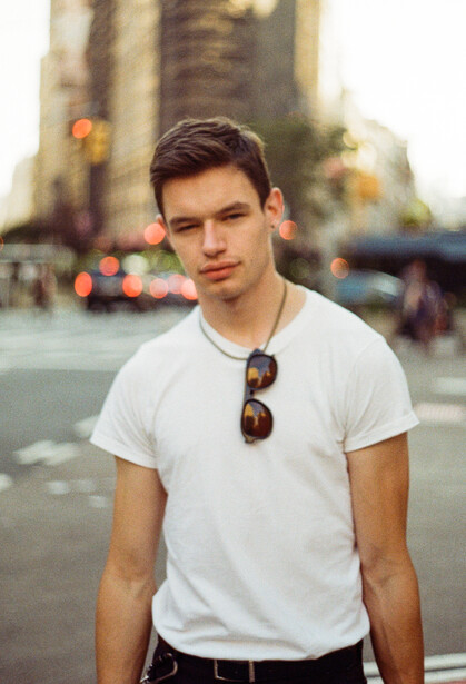 Male portrait subject in white t-shirt with sunglasses on urban street backdrop.