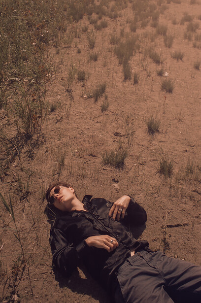 Person lying on arid, sparsely vegetated ground in dark clothing, shot from above.