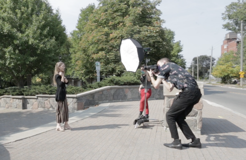 Photographer holding a large reflector during an outdoor portrait shoot with a model in a plaza.