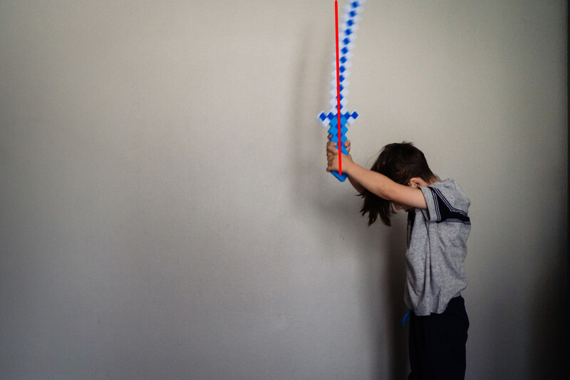 Child reaching toward a beaded string hanging on a white wall.