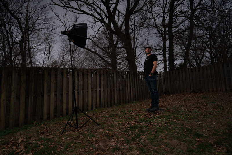 Photographer holding a reflector on a tripod in a bare winter landscape with wooden fence.