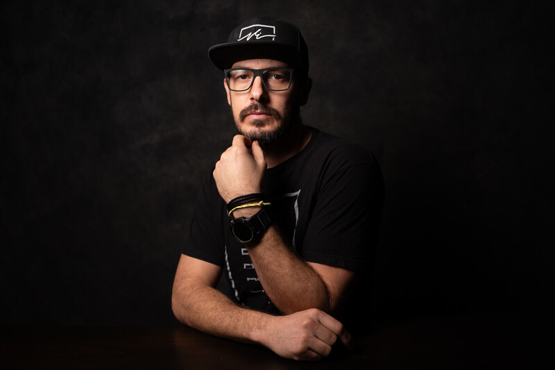 Man wearing glasses and black cap in studio portrait with dark background.