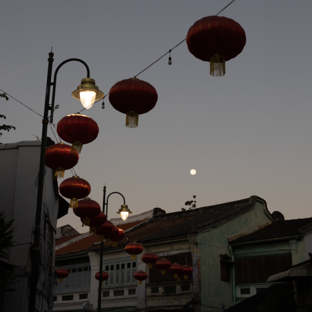 Red lanterns strung along a wire at dusk with traditional architecture visible below.
