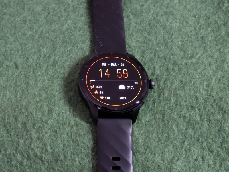 Smartwatch with round display showing time 14:59 and health metrics on green fabric background.