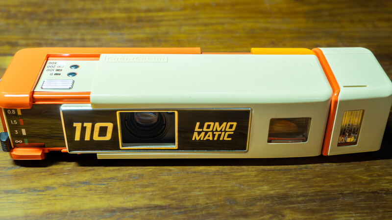 Lomo Fisheye 110 instant camera with orange and white body on wooden surface.