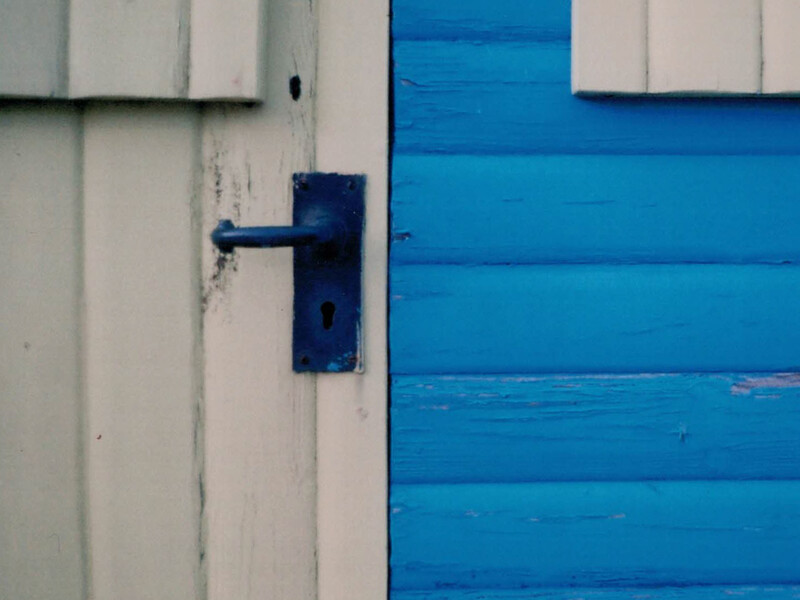Dark blue door handle mounted on white painted wooden door frame beside bright blue wooden panels.
