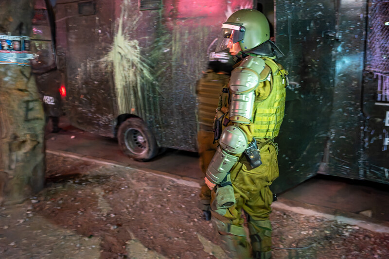 Astronaut in yellow-green spacesuit standing in neon-lit urban alley at night.