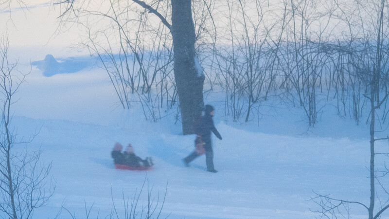 Person pulling a sled through deep snow in a winter forest landscape.