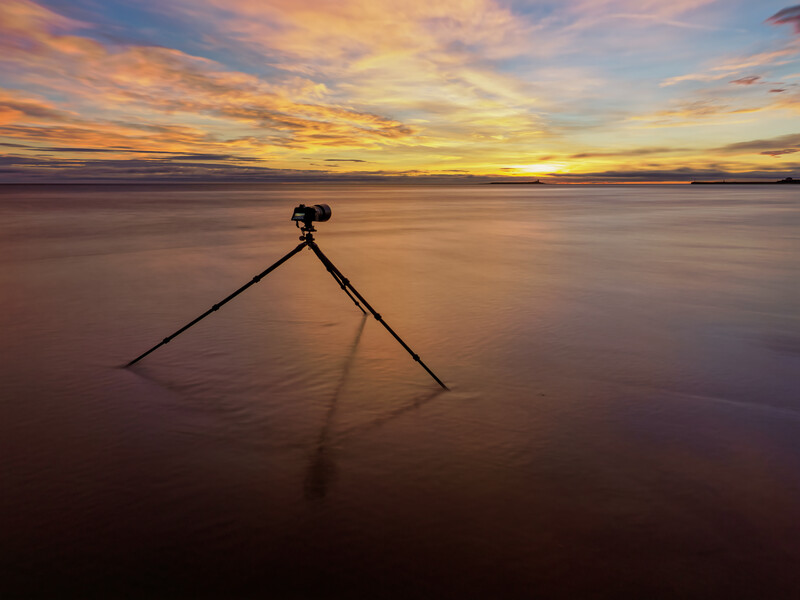 Camera on tripod standing in shallow water during golden hour sunset.