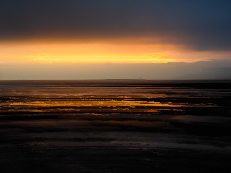 Golden sunset light breaking through dark storm clouds over a calm ocean horizon.