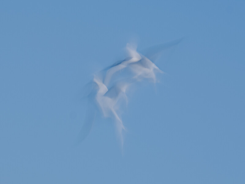 Wind turbine shot from below against clear blue sky, captured with motion blur effect.