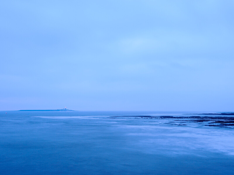 Calm seascape with smooth water and distant horizon under blue twilight sky.