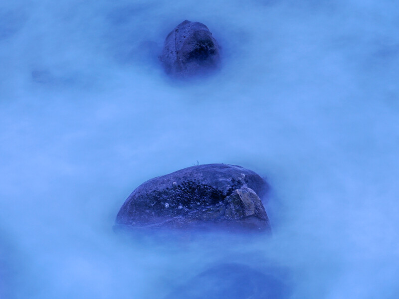 Two dark rocks partially submerged in snow with blue-tinted lighting and soft focus effect.