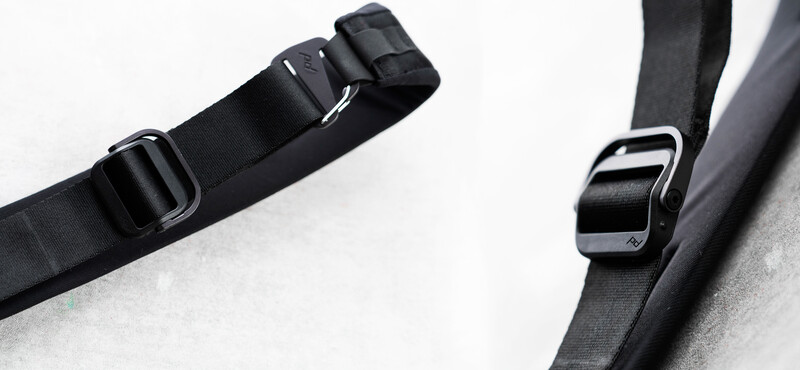 Close-up of two black camera straps with plastic buckle fasteners on white and gray surfaces.