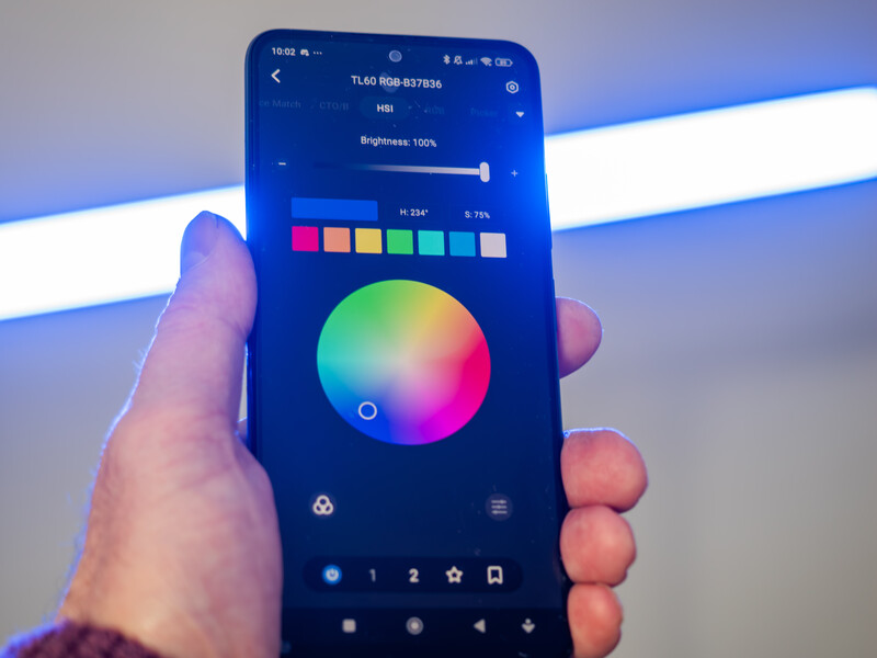 Screenshot of a mobile color picker app displaying a gradient color wheel with brightness slider and preset color swatches.