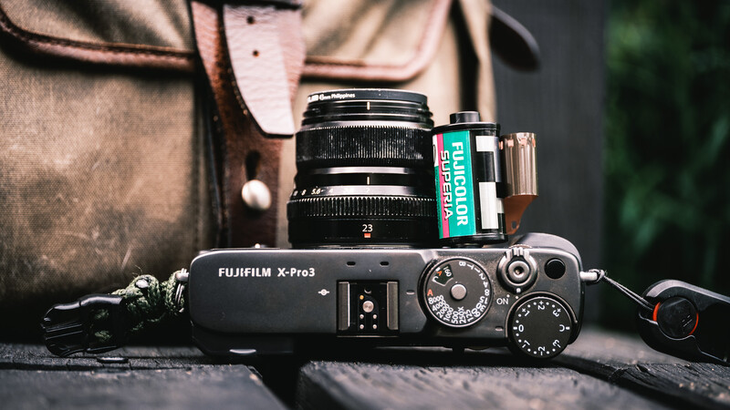 Fujifilm X-Pro3 camera with mounted lens and film box on leather strap.