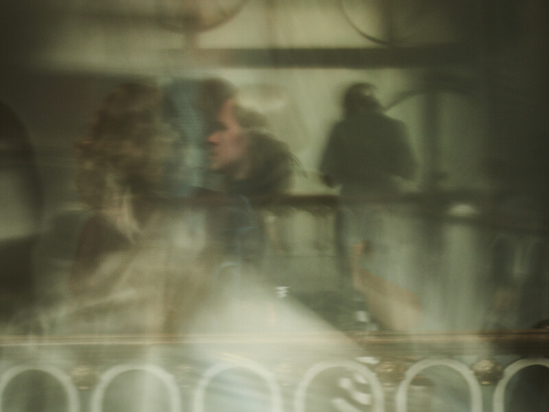 Blurred figures in an interior space with soft, diffused lighting and a muted color palette.