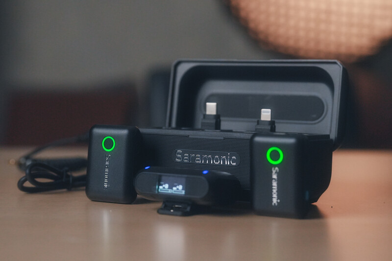 Sennheiser wireless microphone system with two bodypack transmitters and charging dock on wooden surface.