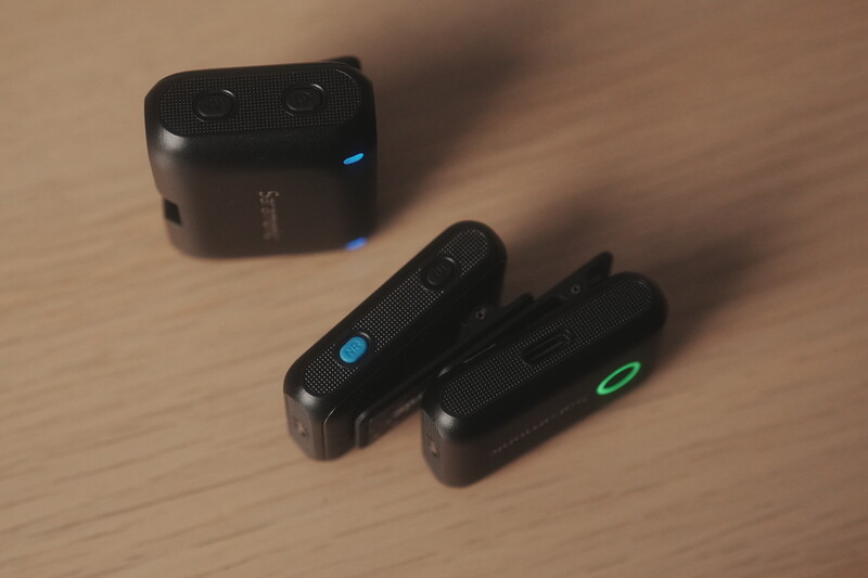 Three black portable audio devices with illuminated indicator lights arranged on a wooden surface.