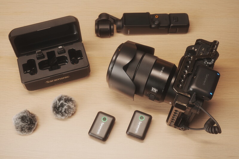 Professional video production equipment laid out on a wooden surface, including camera, lens, microphones, and accessories.