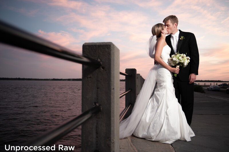 Bride and groom kissing on a wooden pier at sunset, with water and a bridge visible behind them.