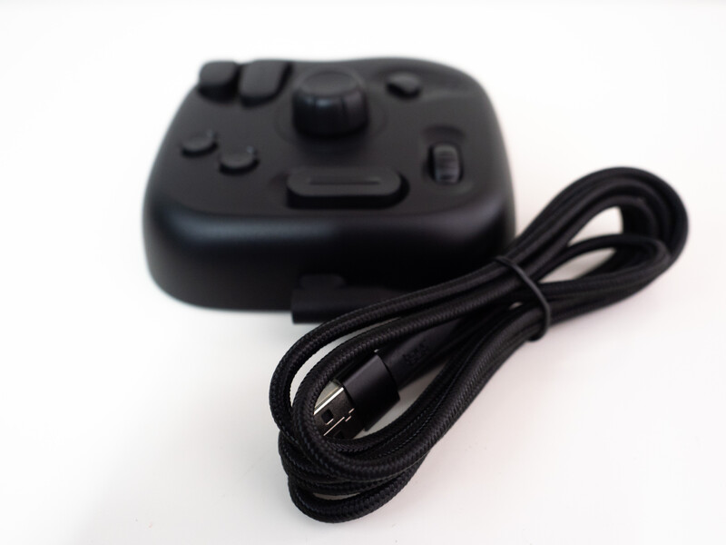 Black gaming controller with coiled cable attached against white background.