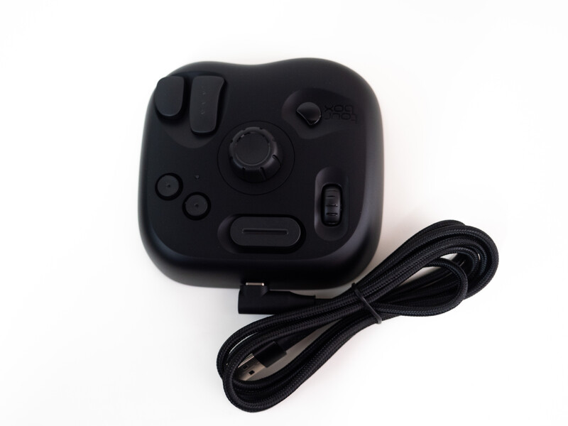 Black compact game controller with attached USB cable against white background.