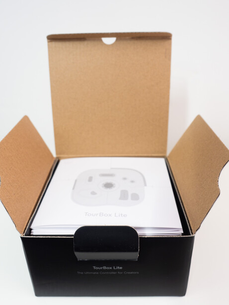 Unboxing shot of a cardboard product box with flaps open, revealing white packaging and black base insert inside.