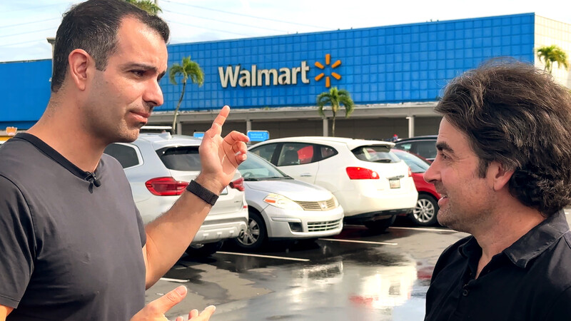 Two men in casual attire having a conversation in a Walmart parking lot on an overcast day.