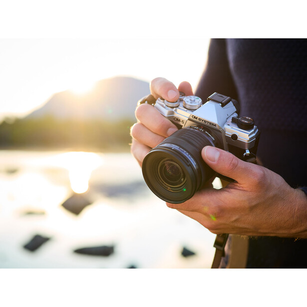 Photographer's hands holding a vintage rangefinder camera with golden lens during golden hour by water.