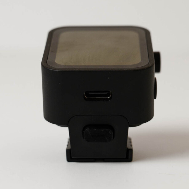 Black compact action camera with small screen viewed from front angle against neutral background.