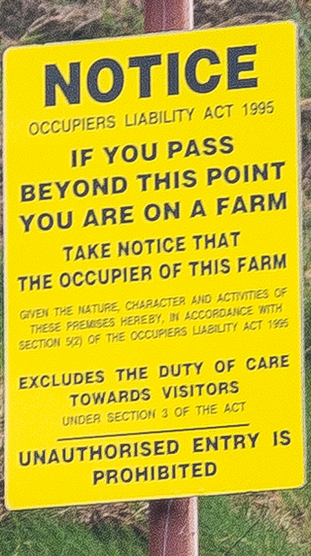 Yellow warning sign attached to wooden post displaying Occupiers Liability Act 1995 notice prohibiting trespassing on private farm property.