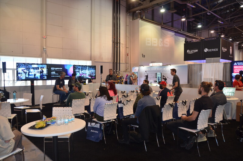 Large conference room with attendees seated at round tables during a panel discussion or presentation event.